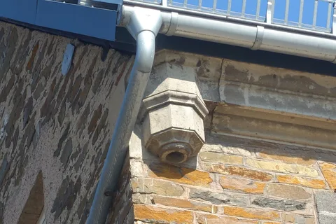 Ancienne gargouille de pierre et gouttière métallique moderne sur la même façade